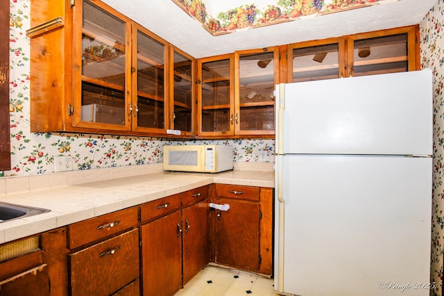 kitchen featuring white appliances, wallpapered walls, and glass insert cabinets