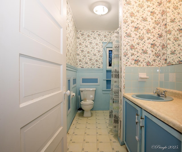 bathroom featuring toilet, a wainscoted wall, wallpapered walls, vanity, and tile patterned floors
