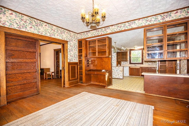 unfurnished dining area with wallpapered walls, wood-type flooring, a chandelier, an ornate ceiling, and a wainscoted wall