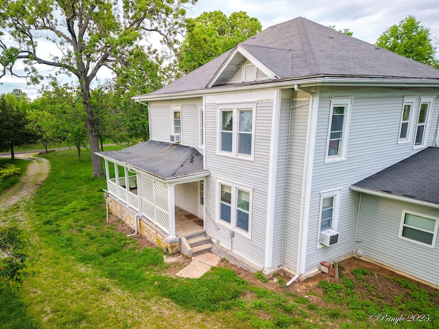 view of side of home featuring a shingled roof, cooling unit, a yard, and covered porch