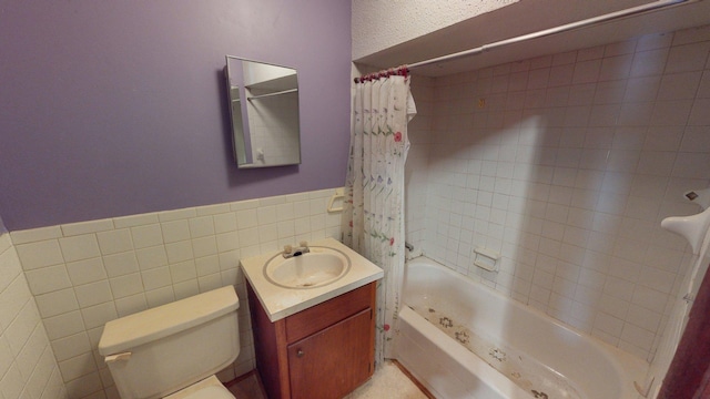 bathroom featuring tile walls, shower / bathtub combination with curtain, vanity, toilet, and wainscoting