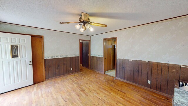 empty room featuring a wainscoted wall, wood finished floors, ceiling fan, a textured ceiling, and wooden walls