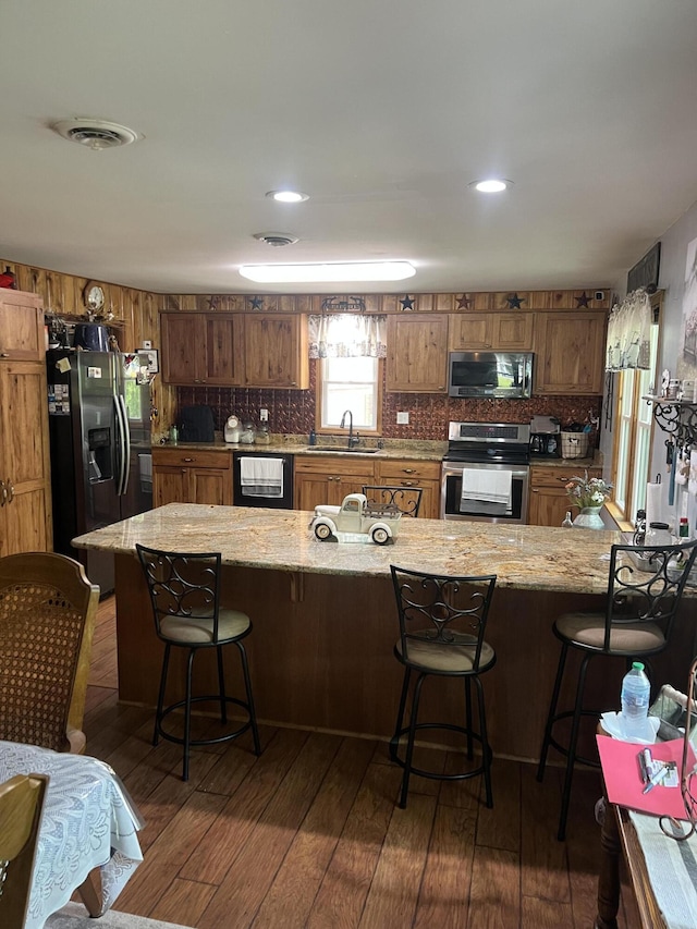kitchen featuring appliances with stainless steel finishes, a sink, brown cabinetry, dark wood finished floors, and a peninsula