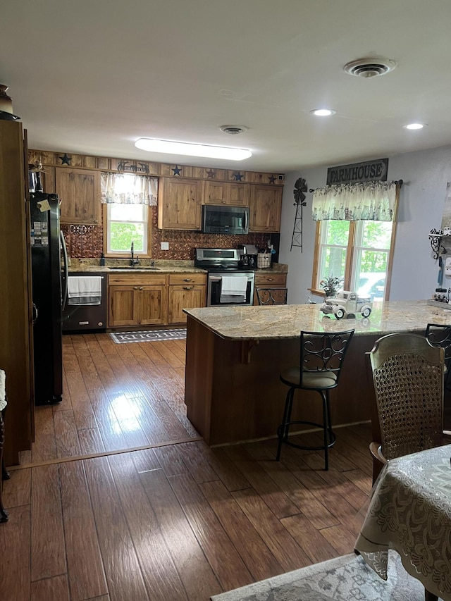 kitchen with stainless steel appliances, brown cabinetry, a sink, dark wood-type flooring, and decorative backsplash