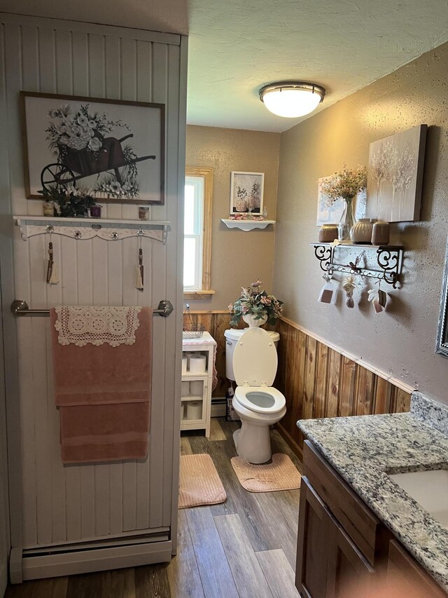 bathroom featuring wood finished floors, toilet, a wainscoted wall, vanity, and wood walls