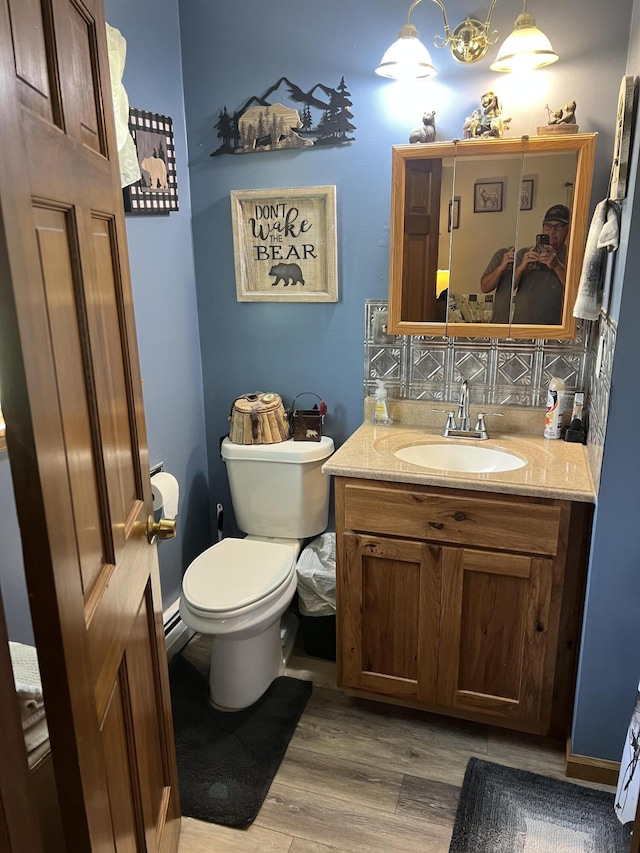 half bathroom featuring wood finished floors, toilet, decorative backsplash, and vanity