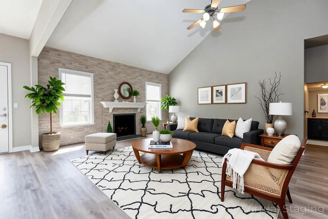 living room with wood finished floors, a ceiling fan, high vaulted ceiling, brick wall, and a fireplace