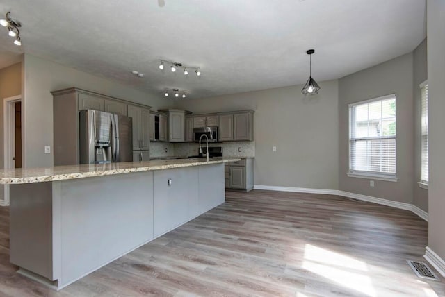 kitchen with stainless steel appliances, light wood-style flooring, backsplash, and a large island with sink