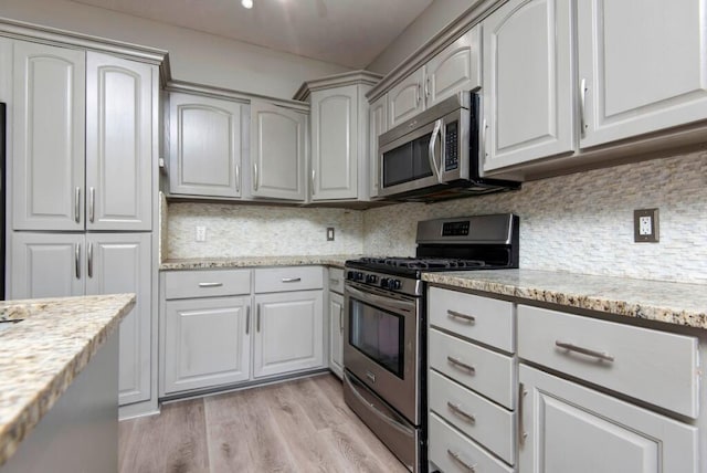 kitchen featuring stainless steel appliances, light wood-style floors, backsplash, and light stone countertops