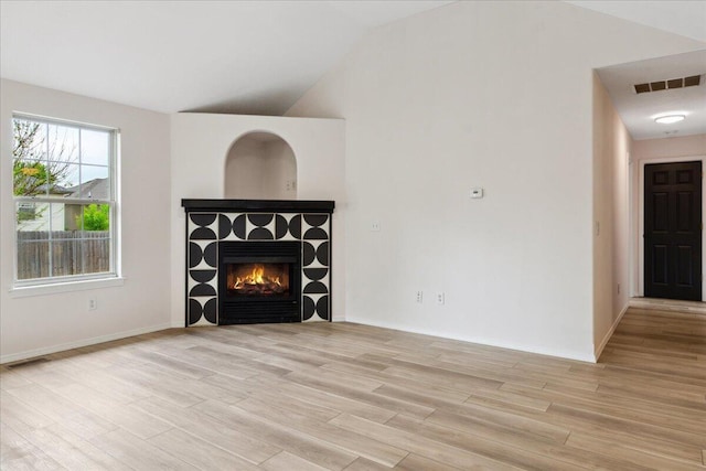 unfurnished living room featuring light wood finished floors, a tiled fireplace, lofted ceiling, and baseboards