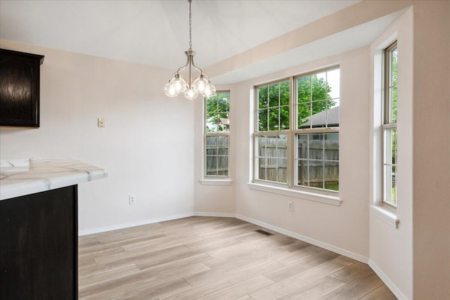 unfurnished dining area featuring light wood finished floors, baseboards, and a chandelier
