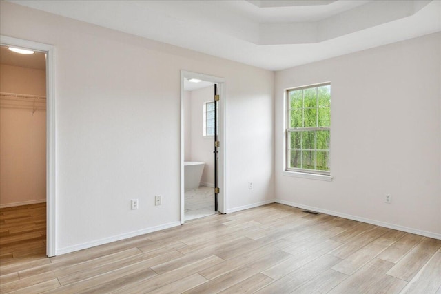 unfurnished bedroom with light wood finished floors, a walk in closet, a closet, baseboards, and ensuite bathroom