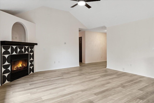 unfurnished living room featuring ceiling fan, a tile fireplace, light wood-style floors, and lofted ceiling