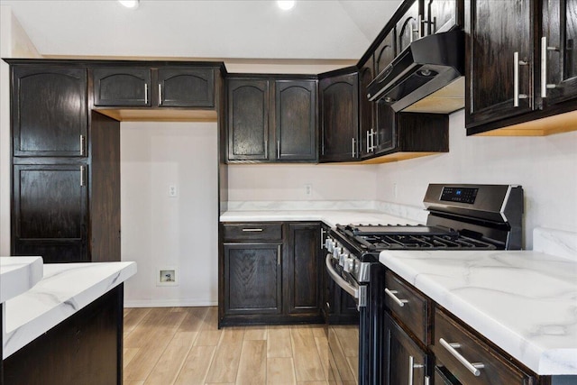 kitchen featuring stainless steel gas stove, under cabinet range hood, light stone countertops, light wood-style flooring, and dark brown cabinetry