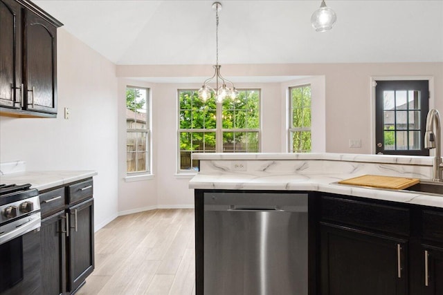 kitchen featuring appliances with stainless steel finishes, light wood finished floors, a sink, vaulted ceiling, and hanging light fixtures