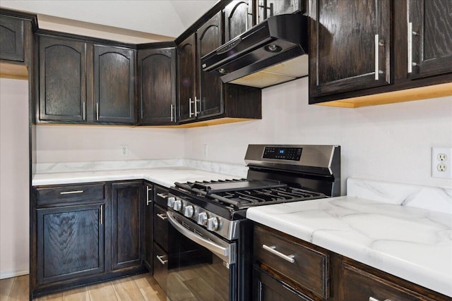 kitchen with stainless steel range with gas stovetop, under cabinet range hood, light stone countertops, light wood-style flooring, and dark brown cabinets
