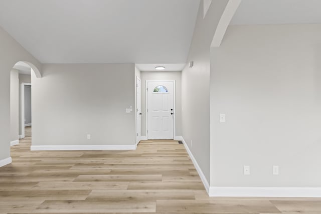 foyer entrance featuring arched walkways, baseboards, and light wood-style floors