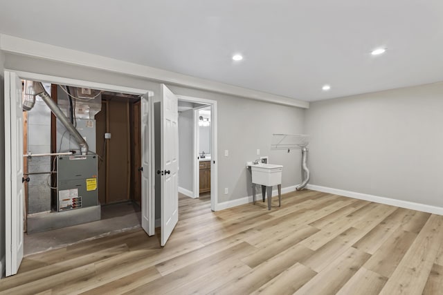 finished below grade area with light wood-style flooring, recessed lighting, baseboards, and a sink