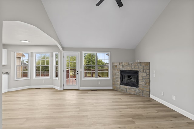 unfurnished living room with ceiling fan, a stone fireplace, light wood finished floors, baseboards, and high vaulted ceiling