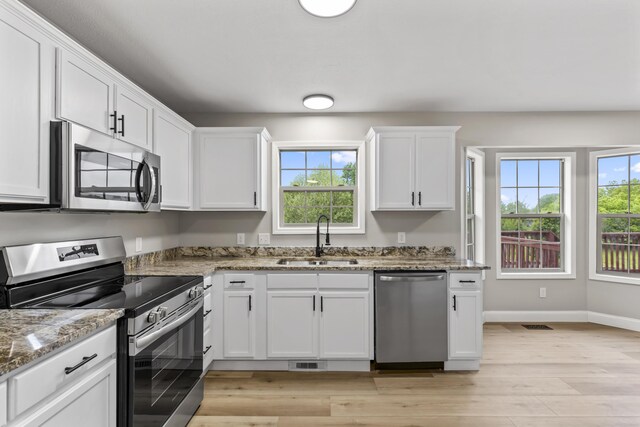 kitchen with stainless steel appliances, a sink, white cabinets, and healthy amount of natural light