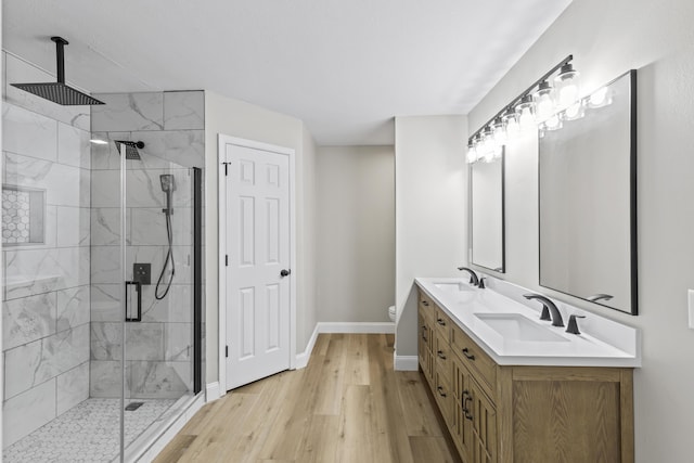 full bath featuring baseboards, wood finished floors, a stall shower, double vanity, and toilet