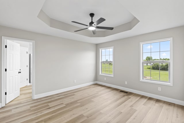 empty room featuring a tray ceiling, light wood-style floors, baseboards, and a ceiling fan