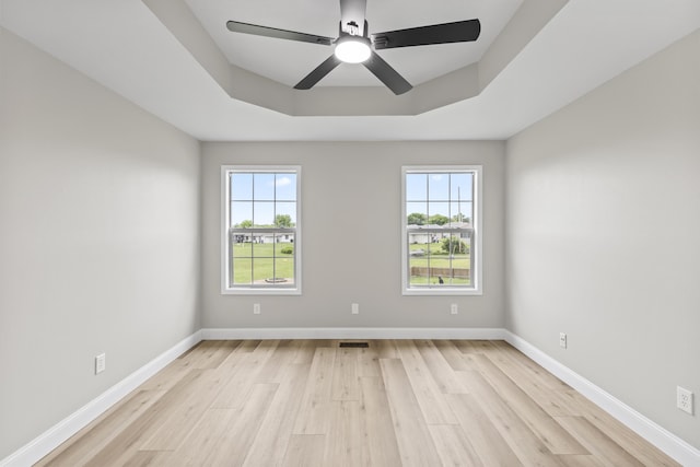 unfurnished room with light wood-type flooring, a ceiling fan, baseboards, and a tray ceiling