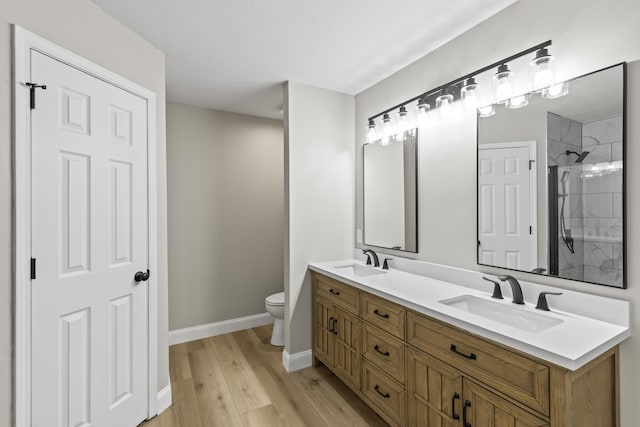 bathroom featuring wood finished floors, baseboards, toilet, double vanity, and a shower