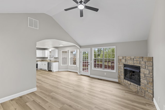 unfurnished living room with arched walkways, a ceiling fan, a stone fireplace, baseboards, and light wood-type flooring