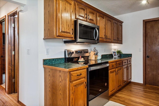1215 E 515th Rd, Morrisville, MO 65710 - kitchen with stainless steel appliances, light wood-type flooring, baseboards, brown cabinetry, and dark countertops