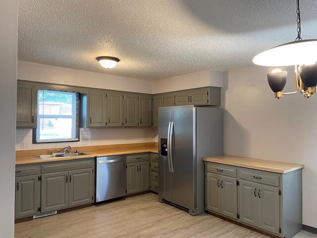 1627 W Lindberg St, Springfield, MO 65807 - kitchen with appliances with stainless steel finishes, gray cabinets, a sink, a textured ceiling, and light wood-style flooring