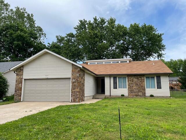 1627 W Lindberg St, Springfield, MO 65807 - view of front of home with an attached garage, concrete driveway, a front lawn, and stone siding