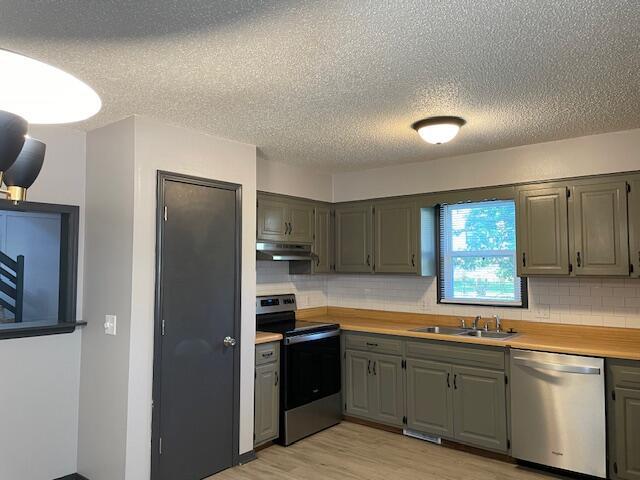 1627 W Lindberg St, Springfield, MO 65807 - kitchen featuring stainless steel appliances, a sink, under cabinet range hood, a textured ceiling, and decorative backsplash