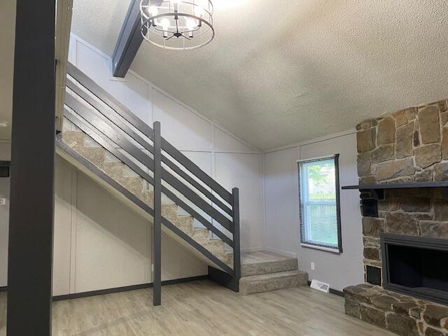 1627 W Lindberg St, Springfield, MO 65807 - stairway featuring a textured ceiling, wood finished floors, a chandelier, a stone fireplace, and lofted ceiling