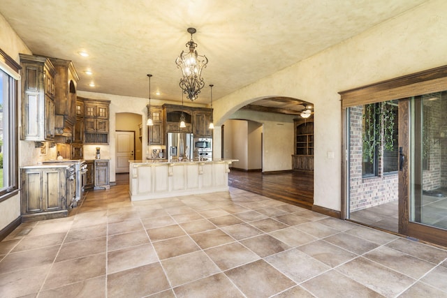 3260 W Rivulet Pass, Springfield, MO 65810 - kitchen featuring appliances with stainless steel finishes, arched walkways, baseboards, a center island with sink, and a chandelier