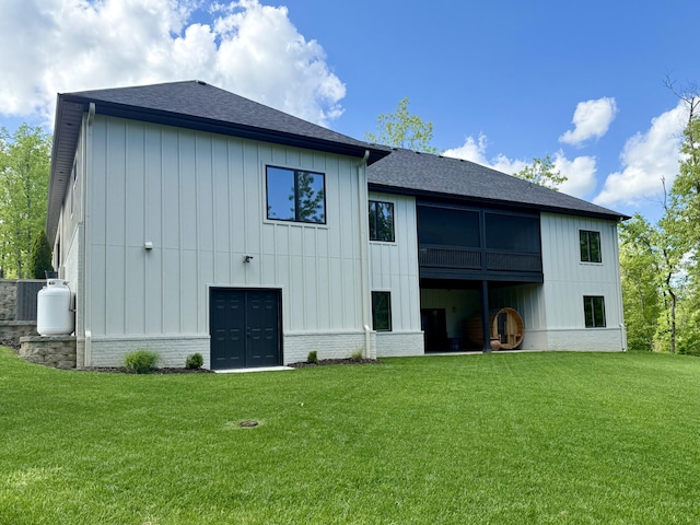 rear view of house featuring board and batten siding, roof with shingles, and a yard