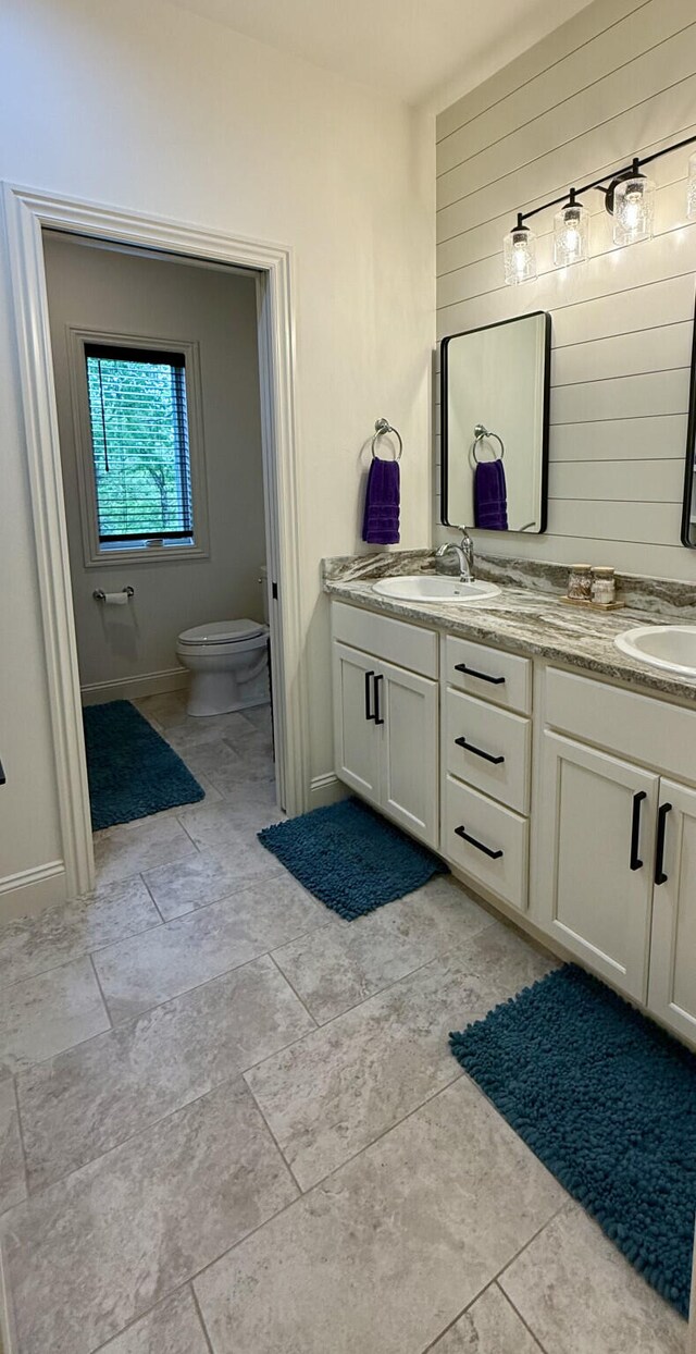 bathroom featuring toilet, double vanity, and baseboards