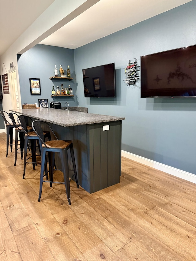 indoor wet bar featuring light wood-style floors and baseboards