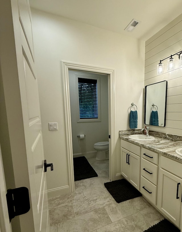 bathroom with toilet, double vanity, and baseboards