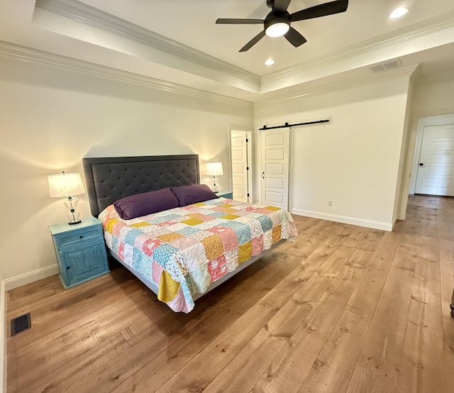bedroom with a barn door, a raised ceiling, ornamental molding, light wood-type flooring, and baseboards