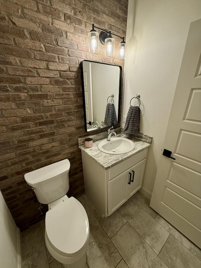 half bath featuring toilet, vanity, tile patterned flooring, and brick wall