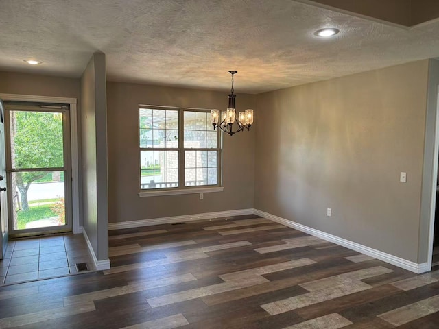 unfurnished dining area featuring baseboards, a chandelier, dark wood-style flooring, healthy amount of natural light, and a textured ceiling