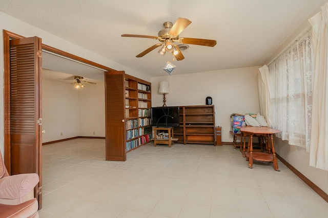 sitting room with ceiling fan, baseboards, and a textured ceiling