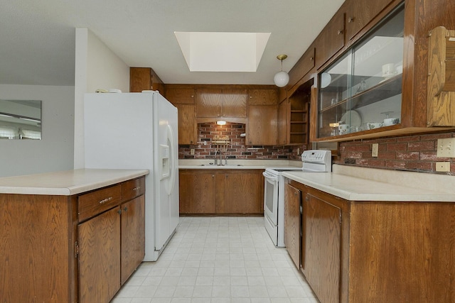 kitchen with white appliances, a sink, a skylight, brown cabinets, and tasteful backsplash