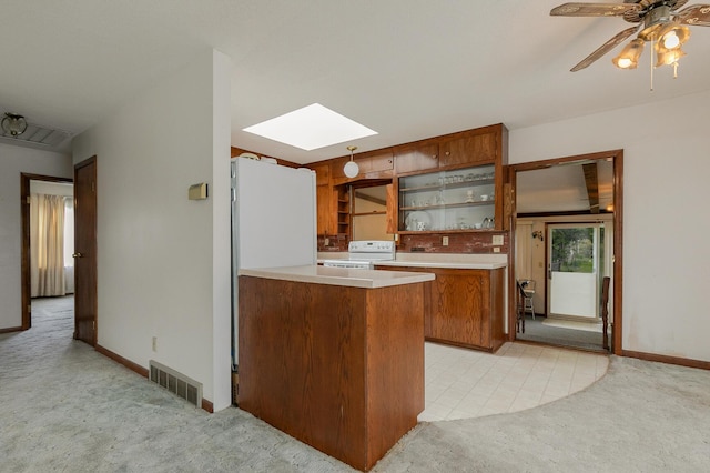 kitchen featuring white appliances, light carpet, brown cabinetry, and a skylight
