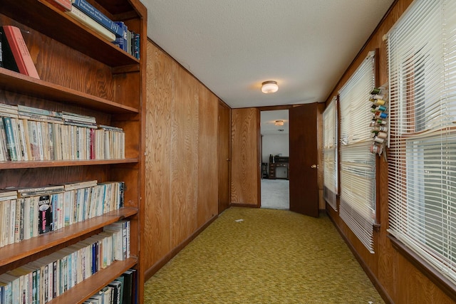 corridor featuring carpet flooring, wooden walls, and a textured ceiling