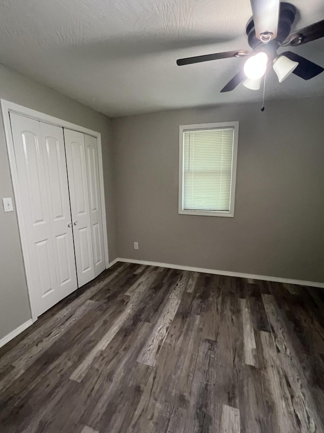 unfurnished bedroom featuring dark wood-style flooring, baseboards, a closet, and a ceiling fan