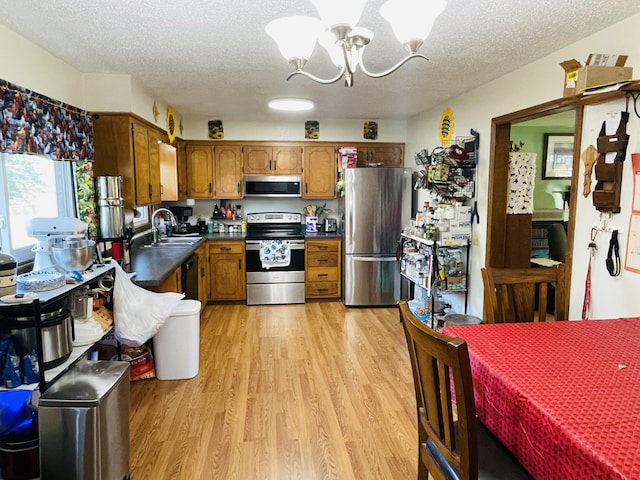 kitchen featuring stainless steel appliances, a chandelier, brown cabinetry, dark countertops, and light wood-style flooring