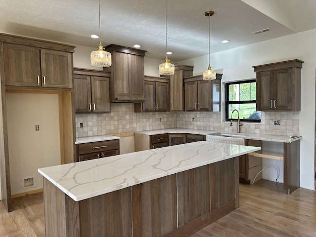 kitchen with light wood finished floors, backsplash, light stone countertops, a sink, and a textured ceiling