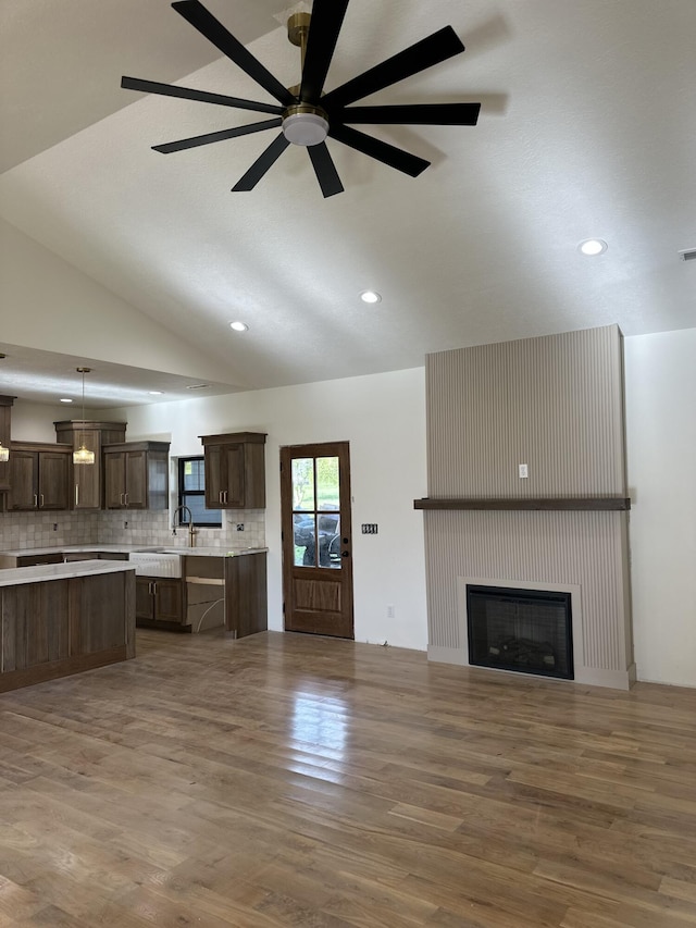 unfurnished living room featuring vaulted ceiling, wood finished floors, recessed lighting, a fireplace, and a sink